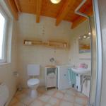 Badezimmer mit Dusche, Waschbecken, Toilette und Holzdecke.