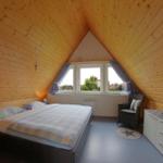 Schlafzimmer mit Holzwand und Dachfenster. Bett, Sessel und Schrank sind vorhanden.