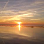 Sonnenuntergang über Watt, Sonne spiegelt sich im Wasser, Himmel mit Streifenwolken.