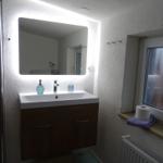 Bad mit beleuchtetem Spiegel, Waschbecken und Fenster.