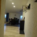 Höhlenförmiger Flur mit Holzboden und Wandgestaltung. Im Hintergrund Essbereich mit Tisch und Stühlen.