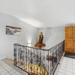 Eingangsbereich mit Treppe, Holzschrank und Skulptur an der Wand.