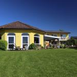 Gelbes Haus mit Garten und Terrasse unter blauem Himmel.