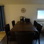 Esstisch mit sechs Stühlen, Wanduhr und Fenster mit Blick auf Leuchtturm.