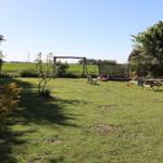 Großer Garten mit Schaukel, Trampolin und Picknicktisch. Blick auf grüne Felder und Windkraftanlage.