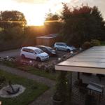 Parkplatz mit drei Autos, Terrasse und Garten bei Sonnenuntergang.