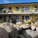 Gelbes Mehrfamilienhaus mit Balkonen und Garten. Große Steine im Vordergrund.