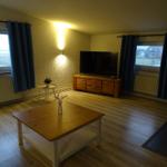 Wohnzimmer mit Holzboden, TV, Tisch und Fenstern mit Blick.