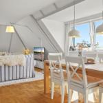 Wohn- und Essbereich mit Holzboden, Sofa, Tisch und Stühle. Große Fenster mit Blick.