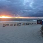 Strand mit Strandkörben und rotem Strandhaus bei Sonnenuntergang.