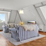 Wohnzimmer mit Sofa, Fernseher und großen Fenstern.