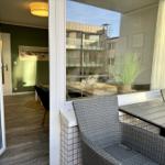 Terrasse mit Tisch und Stühlen. Blick ins Innere mit grünem Wandbereich.