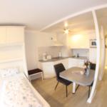 Küche mit Esstisch, Schlafbereich mit zwei Betten und weißer Einbauküche.