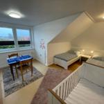 Zimmer mit zwei Betten, Kinderbett und Spielplatz mit Tisch.