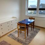 Ein Raum mit Tisch, Stühlen und Schrank. Fenster mit Blick auf Häuser.