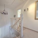 Hallway with stairs, mirror, and chandelier on the wall.