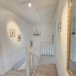 Hallway with stairs, mirror, and ceiling lights. Pictures on the walls.