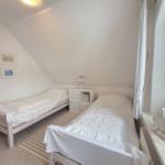 Two beds in an attic room with window and nightstand.