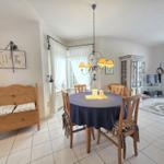 Dining room with round table, wooden chairs, and ceiling fan. Living area with TV and cabinet.