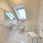Bathroom with shower, toilet, and sink under sloped ceiling.