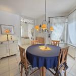 Round table with blue tablecloth and wooden chairs in dining area. Kitchen and bedroom are visible.