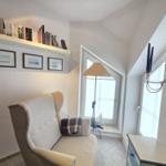 A room with a chair, windows, and a wall shelf with books and decor.