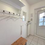 Entryway with coat rack, mirrors, and wooden bench. White door with glass panel.