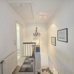 Hallway with stairs, pictures, and chandelier on the wall.