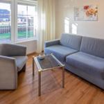 Wohnzimmer mit Sofa, Sessel und Tisch. Fenster mit Blick auf Garten.