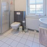 Badezimmer mit Dusche, Toilette und Waschbecken. Fenster und Handtuchhalter sichtbar.