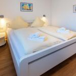 Schlafzimmer mit weißem Bett, Holzboden und Wandbildern.