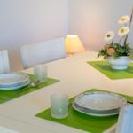 Esstisch mit grünen Untersetzern, Geschirr und Blumenarrangement.