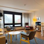 Wohn- und Essbereich mit Sofa, Sesseln und TV. Große Fenster mit Blick.