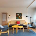 Wohnzimmer mit Sofa, zwei Sesseln und Tisch. Wandbild und Streifenstore.