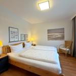 Schlafzimmer mit Doppelbett, Nachttisch, Stuhl und Wandbildern.