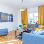Ein Wohnzimmer mit blauem Sofa, gelben Vorhängen und Holzboden.