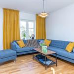 Ein Wohnzimmer mit blauem Sofa, gelben Vorhängen und Holzboden.
