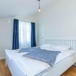 Schlafzimmer mit weißem Bett, blauen Vorhängen und Holzboden.