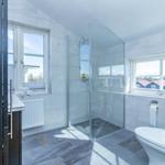 Badezimmer mit Dusche, Toilette und Fenstern zur Aussicht.