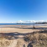 Strand mit Sand, Wasser und blauem Himmel. Ferienhaus direkt am Ufer.