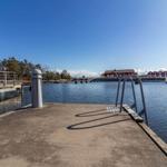 Hafenbecken mit Steg, roten Häusern und klarem Himmel.