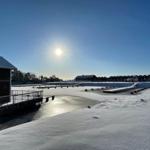 Schneebedeckter Hafen mit Bootshäusern und klarem Himmel.