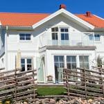 Weiße Villa mit rotem Dach, Balkon und Holzzaun vor grünem Grund.