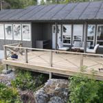 Holzterrasse mit Sitzgelegenheiten und Grill vor einem Haus mit grauer Fassade.