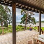 Terrasse mit Blick auf Wasser und Bäume. Holzbank mit Kissen und Pflanze.