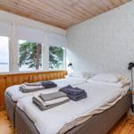 Schlafzimmer mit Doppelbett, Fensterblick auf Wasser und Bäume, Holzdecke und -boden.