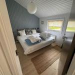 Bedroom with bed, window, and wooden floor. Ceiling and walls are paneled.