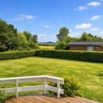 Behind a lawn with hedge stands a wooden house. View of water and trees.