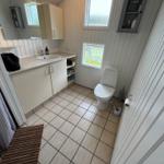 Bathroom with sink, toilet, and shower. White walls and tiles.