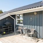 Terrasse mit Tisch, zwei Stühlen und Grill. Holzdecke, graue Wand und Fenster.